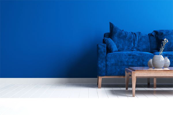 Blaue Couch mit Wohnzimmertisch vor blauer Wand.
